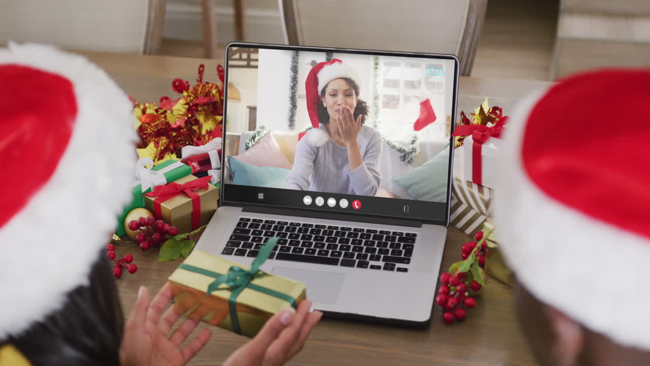 pareja diversa con sombreros de santa teniendo llamada de video portátil con mujer biracial