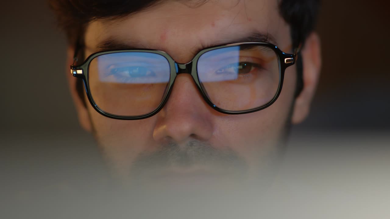 primer plano de un apuesto hombre de negocios con gafas mirando la pantalla de la computadora usando una computadora de escritorio trabajando de noche en la oficina.