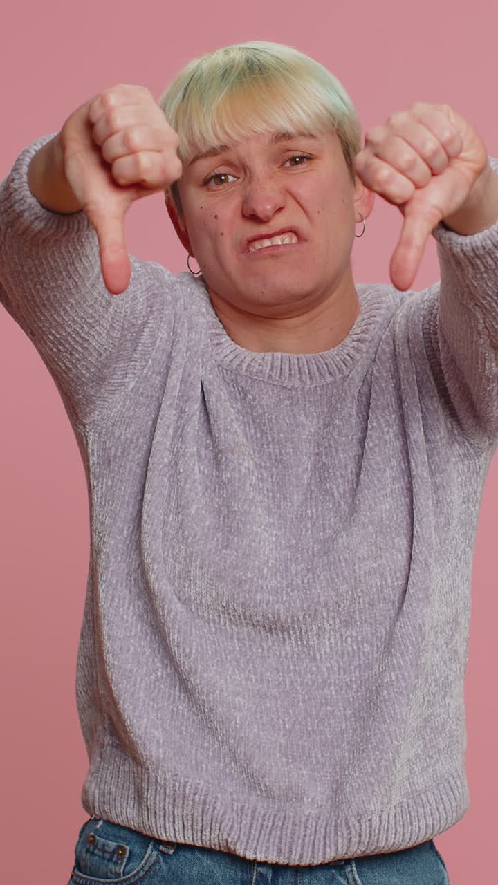 Upset woman in white sweater showing thumbs down sign gesture disapproval dissatisfied dislike