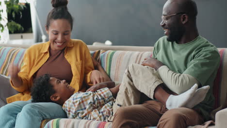 happy african american parents ticking little son on sofa at home