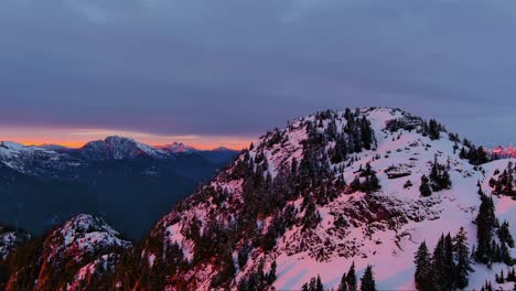 snow-covered mountain peaks with trees. dramatic pink sunset sky, winter season. canadian nature, aerial cinematic. british columbia, canada
