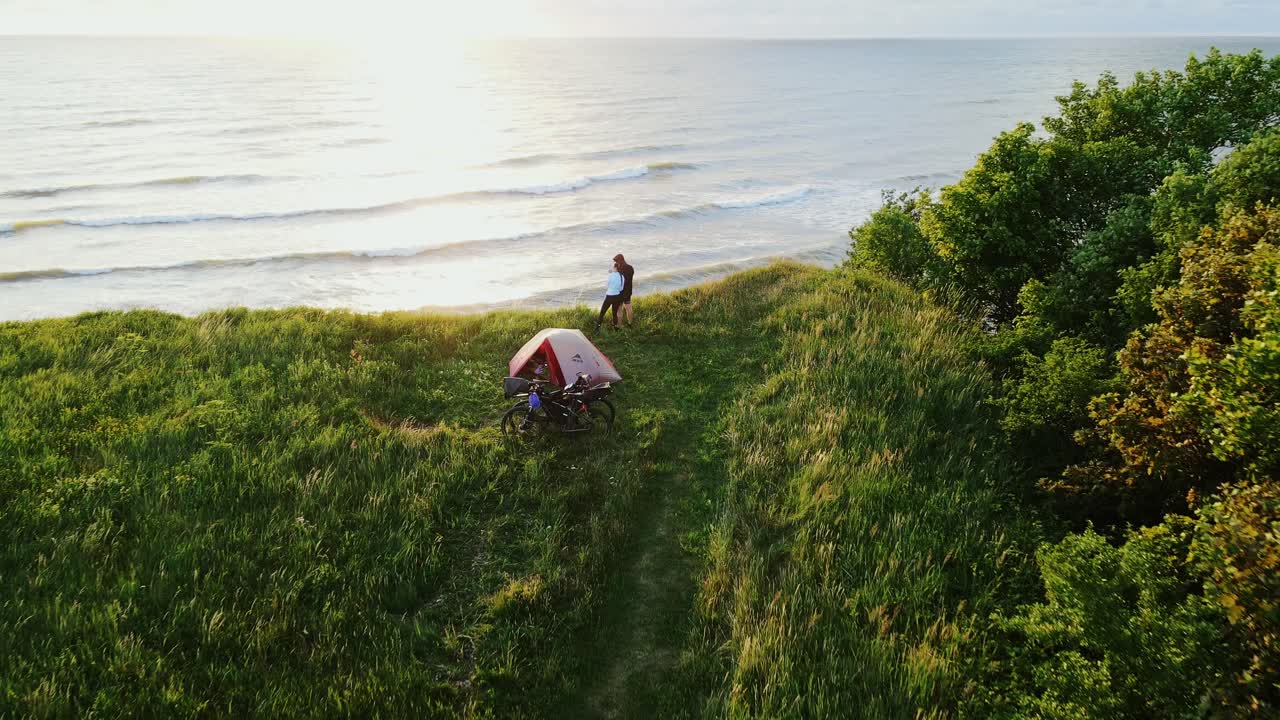 Adventurous couple camping on a stunning Baltic Sea cliff, watching sunset glow