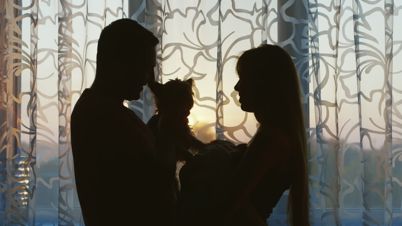 창가에 서 있는 아이와 개가 있는 행복한 가족 아버지는 개 어머니 브레아를 손에 들고 있습니다