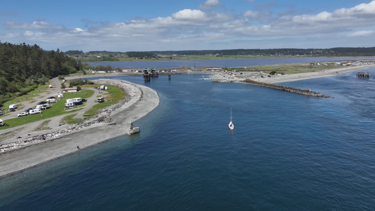 Wide drone shot following a sailboat traveling back to the boat ramp.
