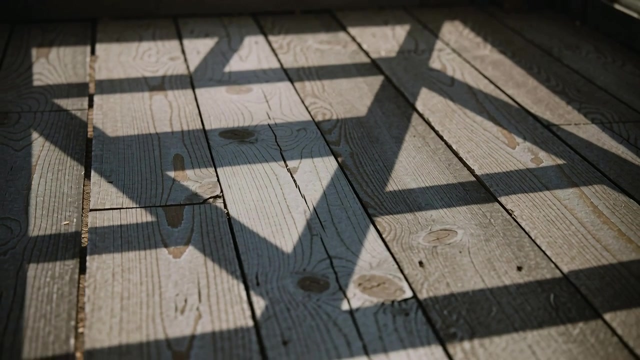 Shifting geometric shadows sliding across worn plank floor at sunroom, from sun through window grid