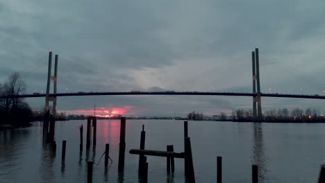 Drohnen-4K-Aufnahmen-Von-Alex-Fraser-Bridge,-Aufnahme-Einer-Modernen-Hängebrücke-Aus-Einem-Niedrigen-Winkel,-Während-Man-über-Ein-Altes,-Kaputtes-Dock-Fliegt-Und-Dabei-Den-Sonnenuntergang-Sieht,-Während-Autos-Und-Lastwagen-Die-Brücke-überqueren