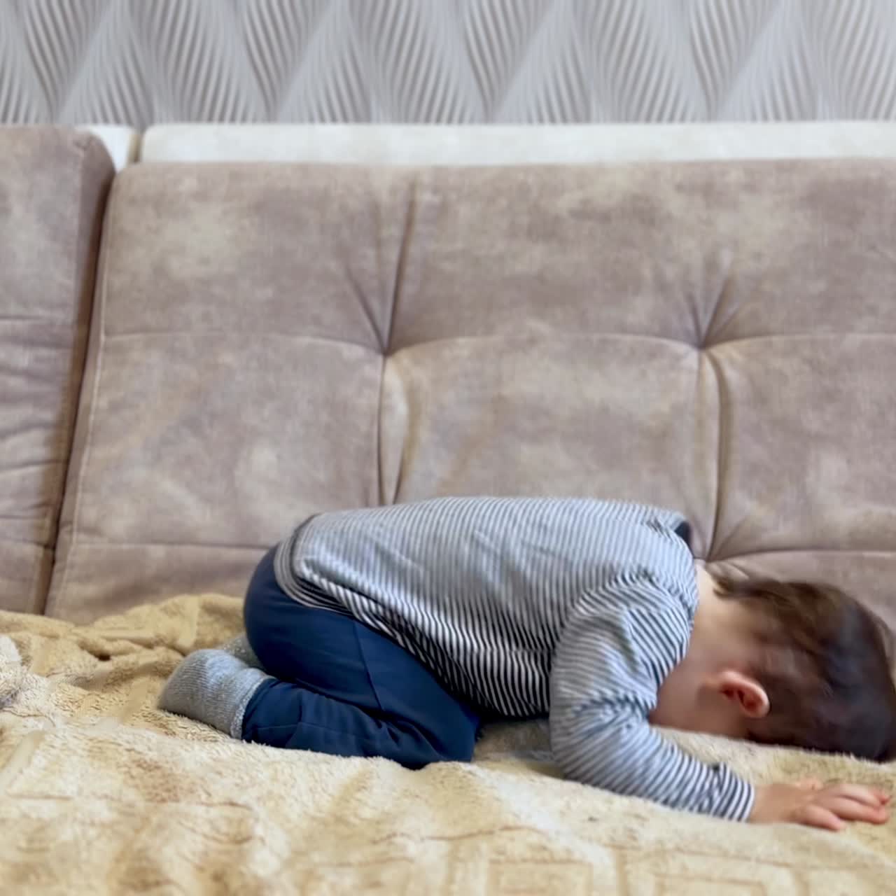 Beautiful active Caucasian toddler having fun jumping on the sofa. Kid waves his hands excitedly and smiles adorably