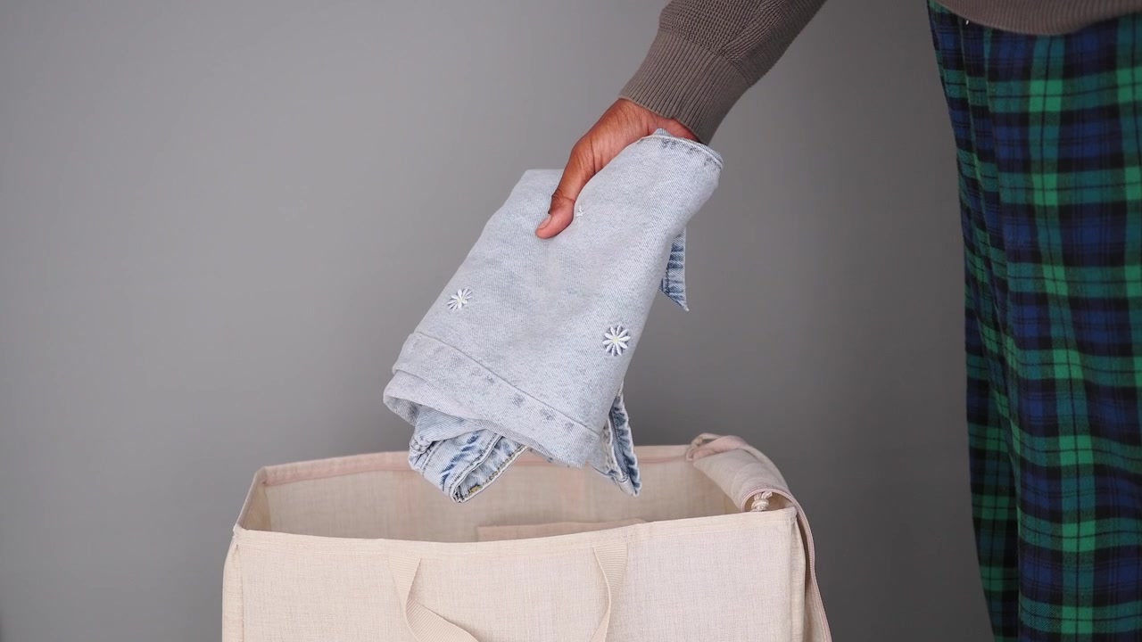 Person Placing Folded Jeans into a Laundry Basket