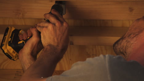 Closeup-of-Bearded-Man-Drilling-Hole-With-Power-Drill-Into-Big-Piece-of-Wood-In-Workshop