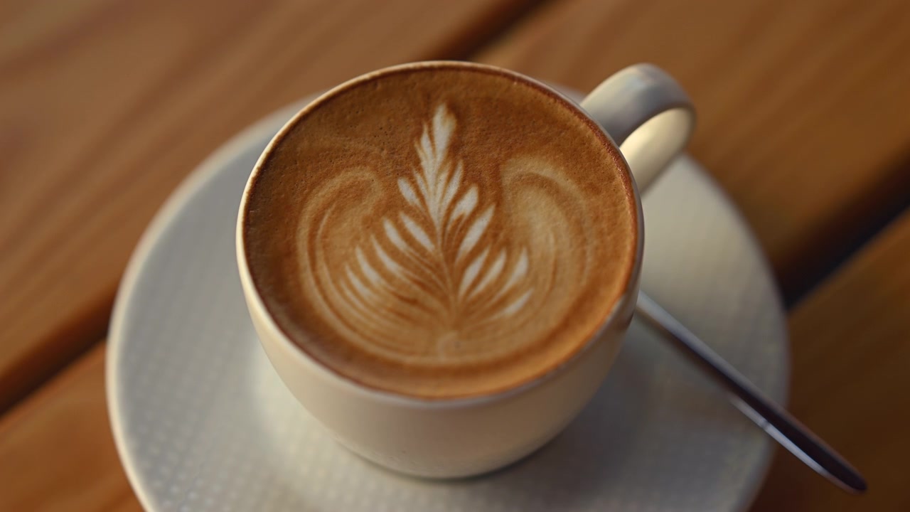 Latte macchiato appena preparato servito in una tazza di ceramica con un'elegante latte art a forma di foglia su schiuma cremosa