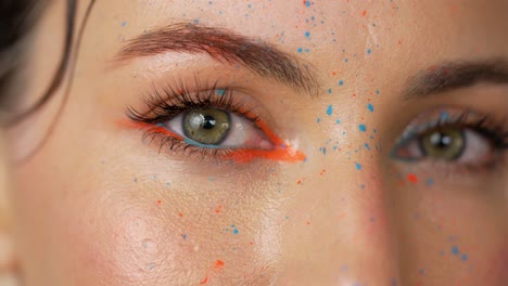 close-up of a woman's face with colorful makeup and paint splatters.