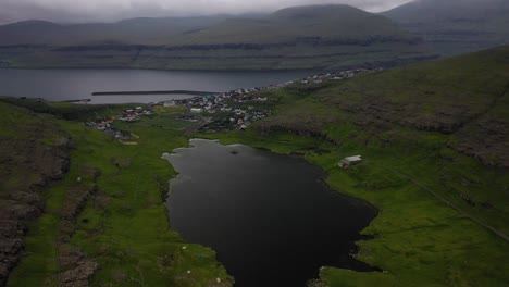 small coastal fishing village in faroe islands setting, cloudy aerial pull-back