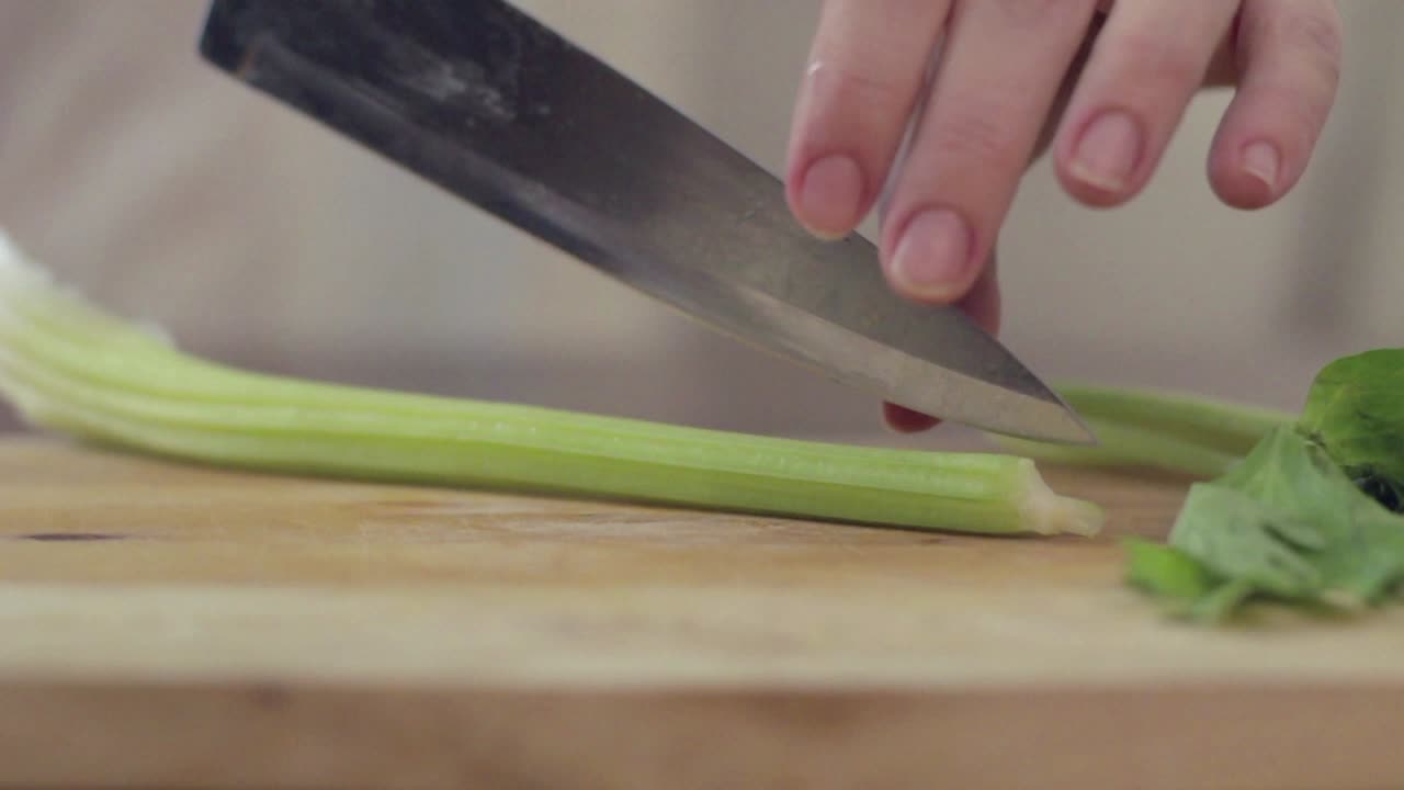 Primo piano di una mano che taglia sedano fresco su un tagliere di legno