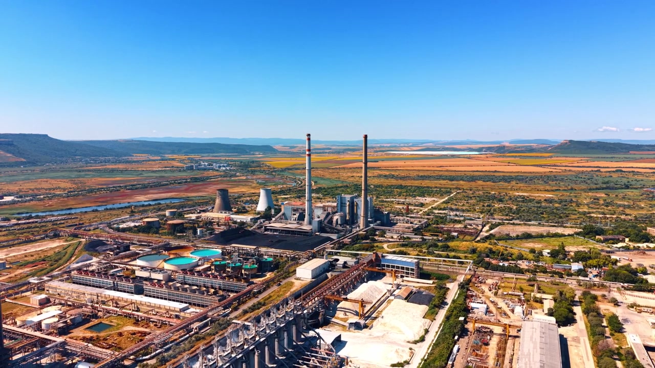 Usina elétrica perto de rio e campos. Vista aérea de uma usina elétrica com chaminés junto a um rio e campos, exibindo a paisagem diurna