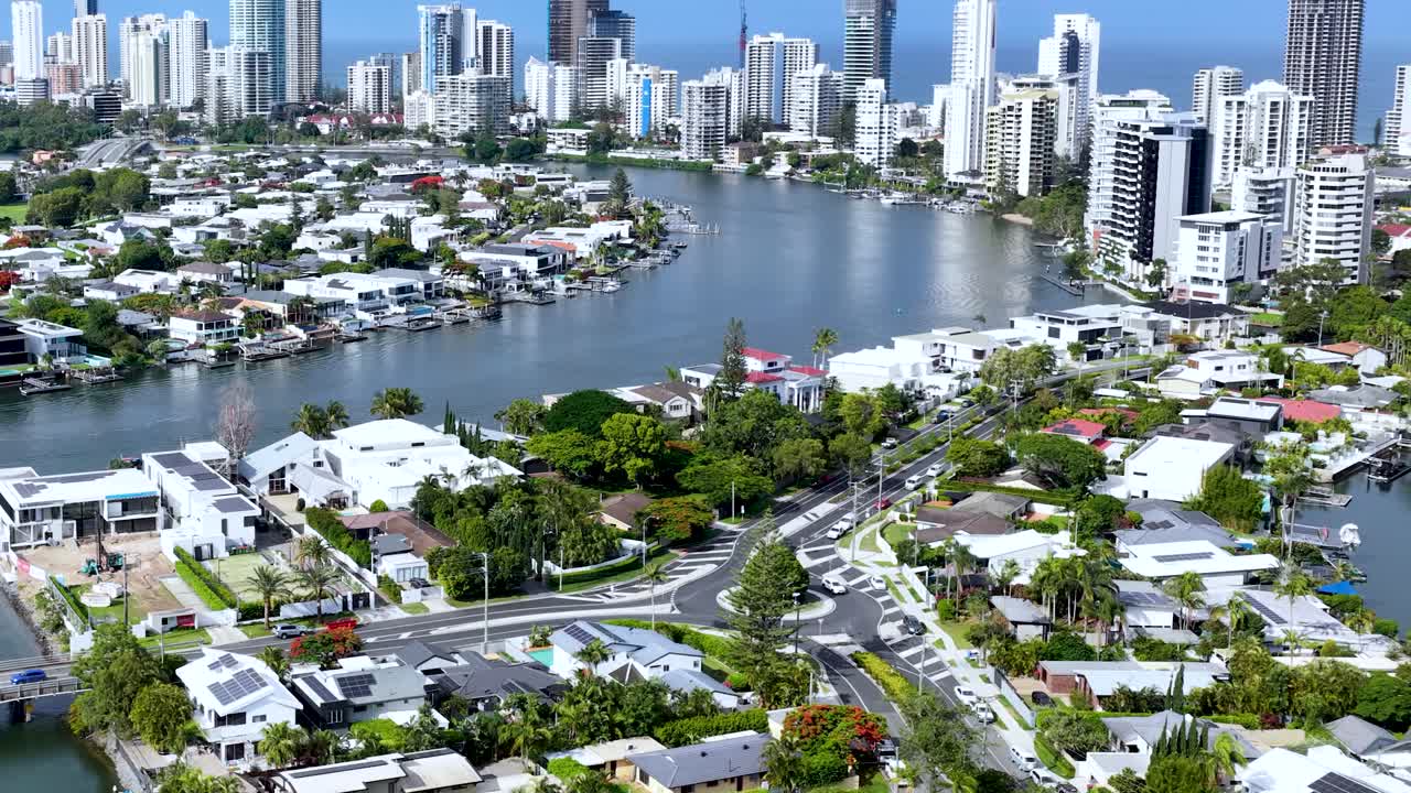 Drone glides above canal-side luxury homes toward Gold Coast skyline, bright daylight, smooth movement