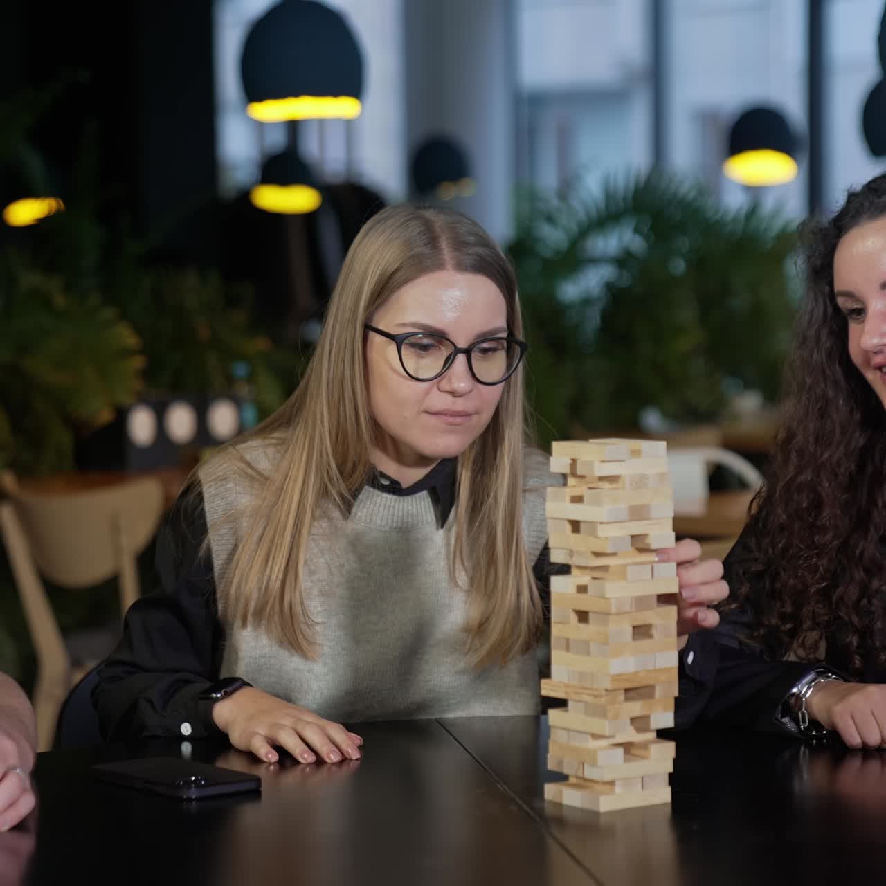 Group of colleagues playing jenga during the lunch break. Two women and man sitting at the table and playing board game in cafeteria