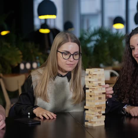 group of colleagues playing jenga during the lunch break. two women and man sitting at the table and playing board game in cafeteria