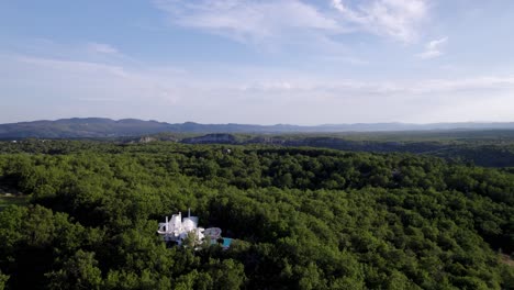 aerial tilt view of a white "bubble house" and its pool in the middle of a forest in southern france