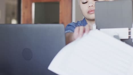 mujer biracial ocupada trabajando en casa con computadora portátil en cámara lenta