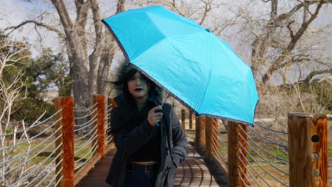 una mujer bonita caminando con un paraguas azul a través de un puente durante el mal tiempo y una tormenta de lluvia a cámara lenta