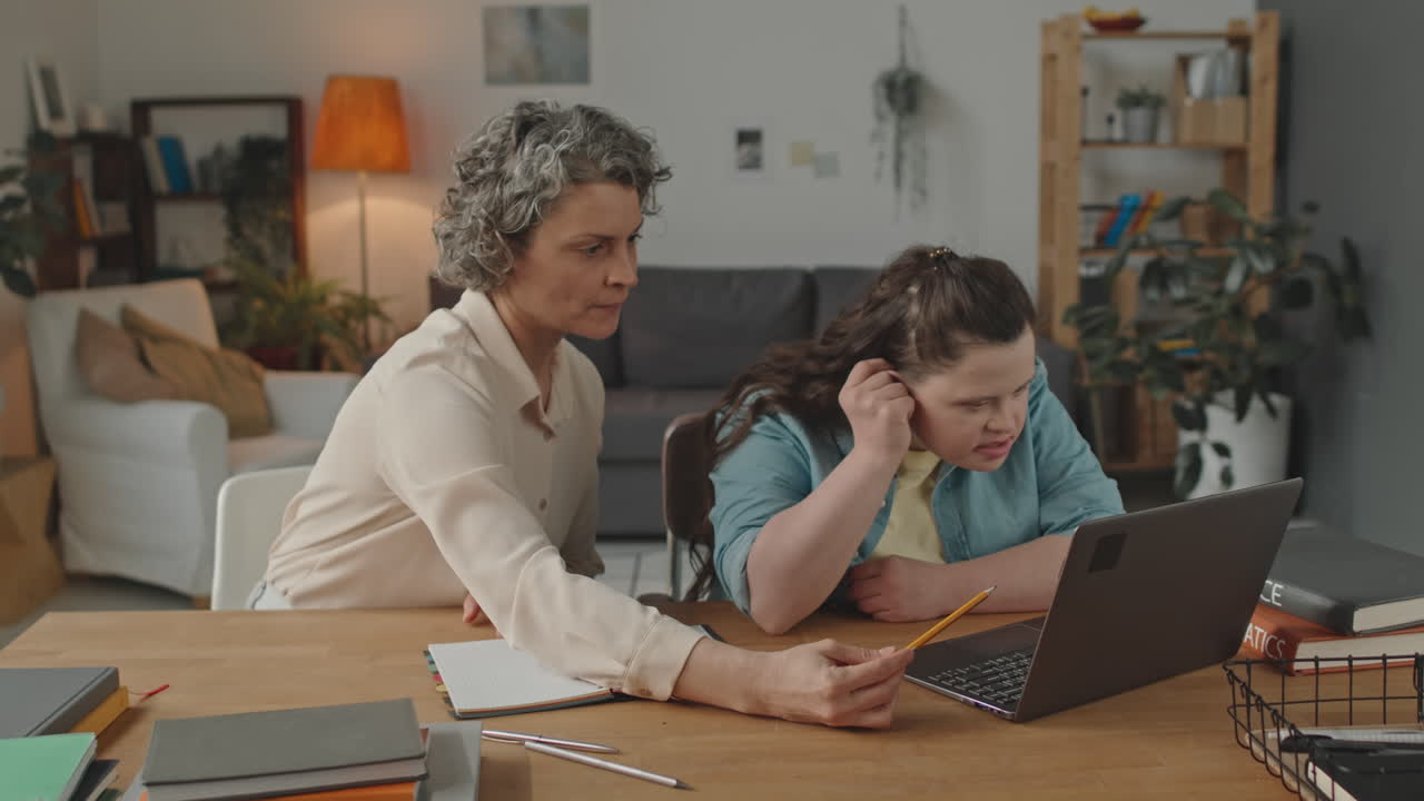 Woman teaching a person with down syndrome how to use a laptop
