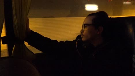 a tired young man with headphones looking out of a bus, a flixbus, while it rides through a tunnel