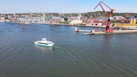 Small-passenger-ferry-crossing-Gota-Alv-in-Gothenburg,-Sweden-on-a-sunny-day-with-the-old-ship-yard-cranes-on-Hisingen-in-the-background