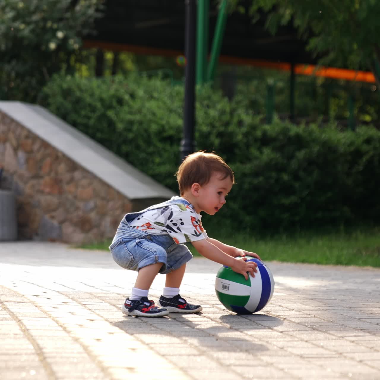 Rear view of a baby boy coming up carefully to the ball. Adorable kid picks up a ball and runs with it happily smiling. Low angle view