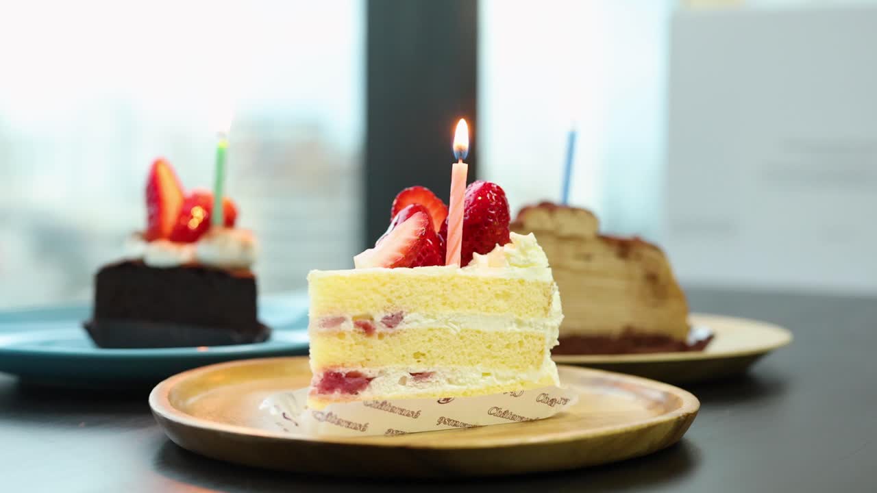 Hand lights candle on strawberry shortcake, cakes on table, bright natural daylight, steady camera