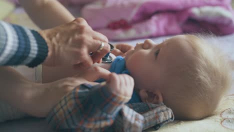 pediatrician listens to baby lungs with stethoscope on bed