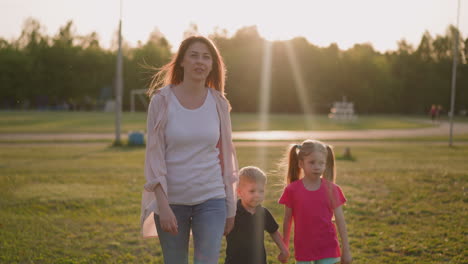 Happy-woman-and-little-kids-walk-along-city-park-in-evening