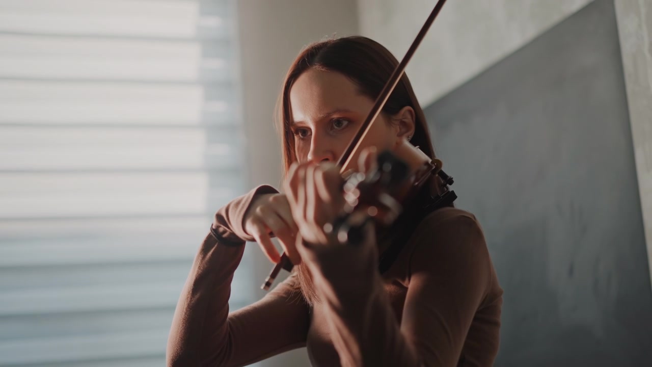 Violinista coscienzioso si concentra sul perfezionamento delle tecniche di esecuzione. Musicista intensamente concentrato lavora su un'espressiva diteggiatura durante una rigorosa sessione di pratica con luce naturale dalla finestra