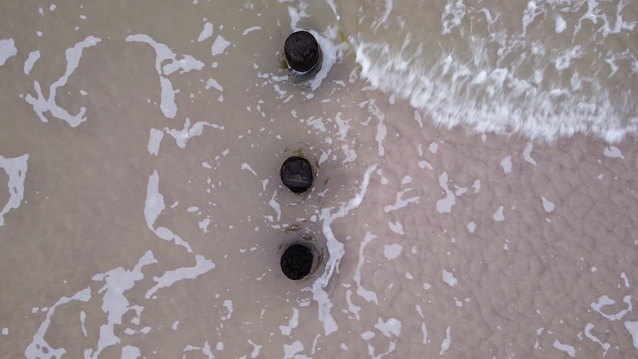 발트해 해안선에 있는 오래된 목조 부두의 아름다운 공중 전망, 흐린 날, 해안 침식의 영향을 받는 하얀 모래 해변, 고요한 해변, 넓은 낮은 각도의 버드아이 드론 샷