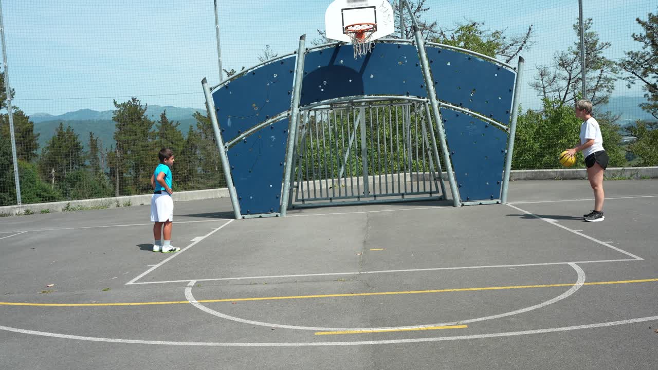 Donna e ragazzo giocano a basket su un campo all'aperto