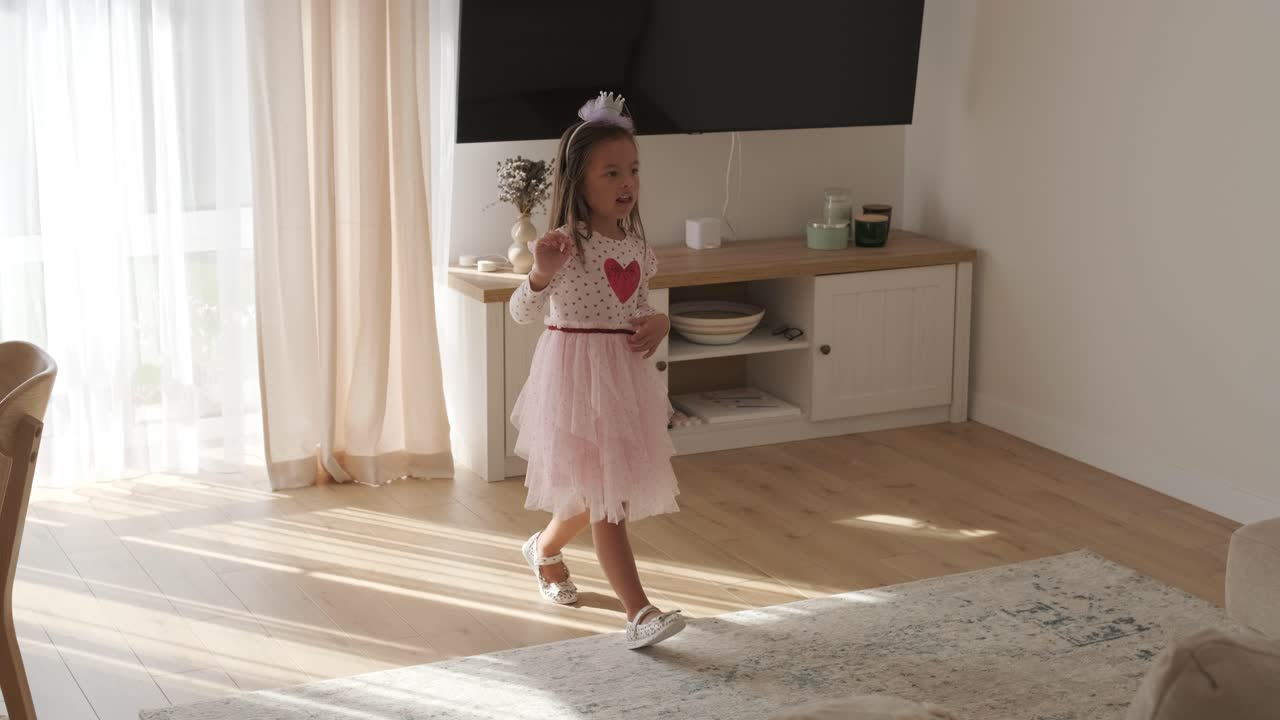 una joven baila alegremente en una sala de estar luminosa y acogedora. lleva un vestido rosado con un diseño de corazón, moviéndose juguetón en el espacio minimalista iluminado por el sol con decoración neutral y luz natural suave.