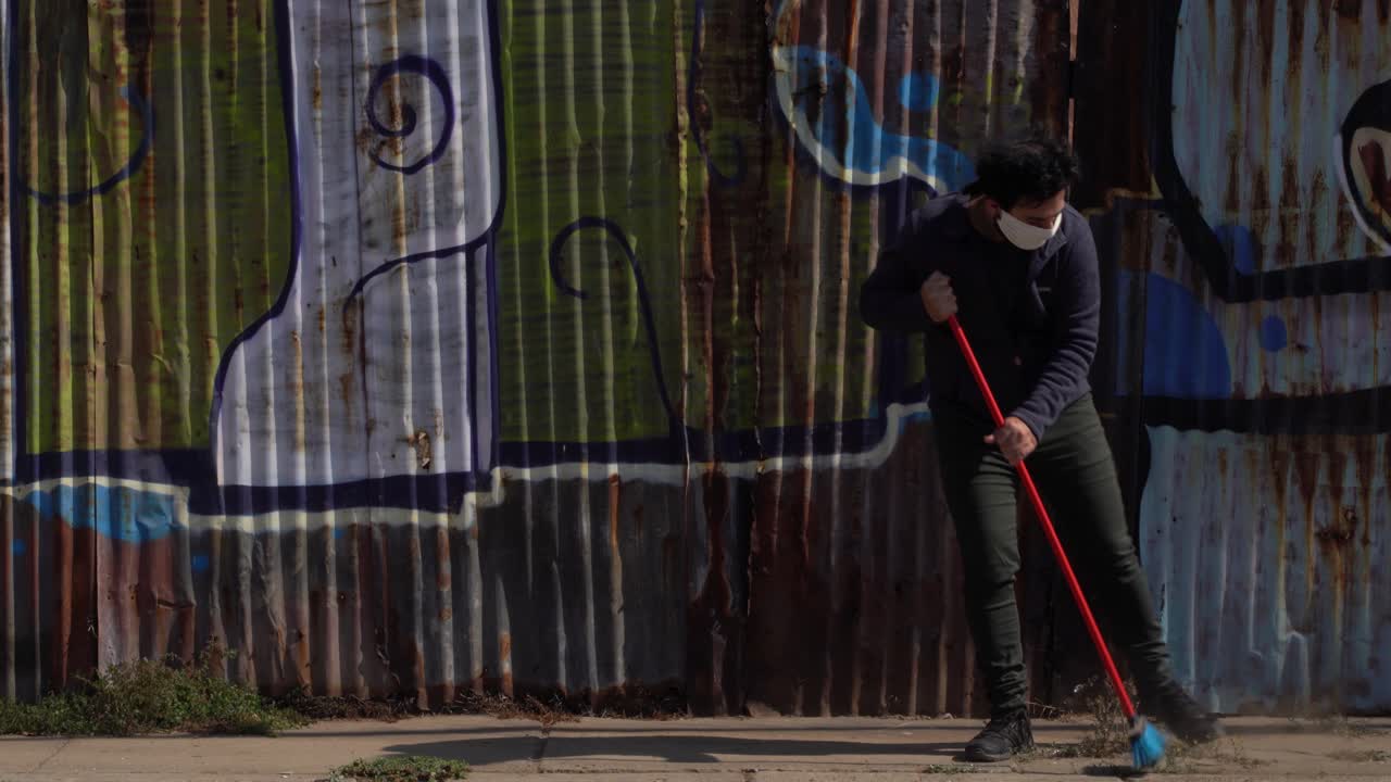 hombre con mascarilla desechable barre la calle, polvo sucio en el aire