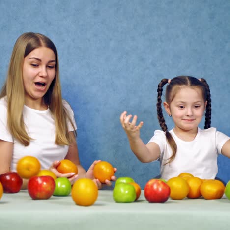 woman and little girl playing with fresh fruits at home. mother and daughter juggle with orange tangerines. organic fruits on the table.