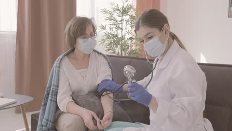 female doctor takes the pulse of an elderly patient sitting on a sofa 2