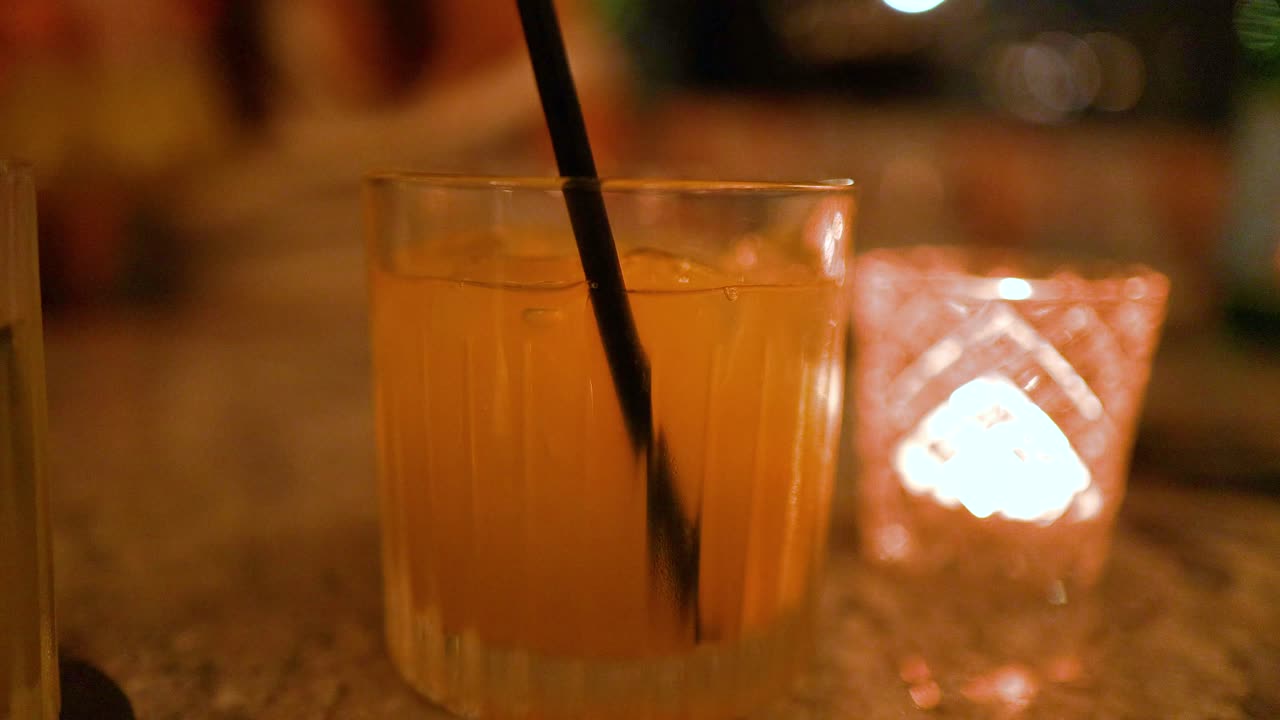 A hand stirs a cocktail on a dimly lit bar counter, creating a warm, intimate atmosphere