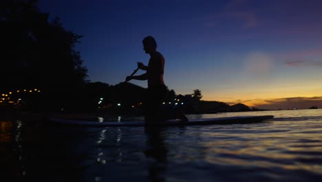 silhouette of a person paddleboarding at sunset