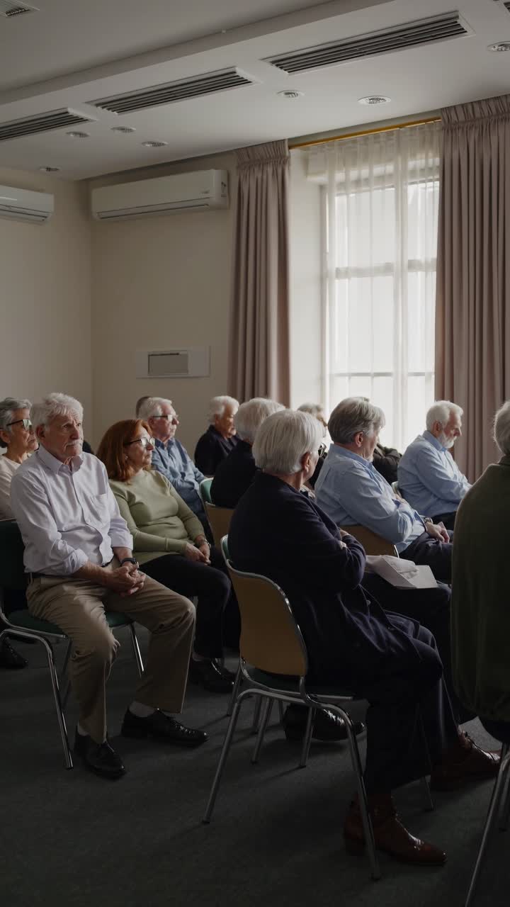 Un gruppo di anziani seduti in una sala seminari, visti da un angolo laterale