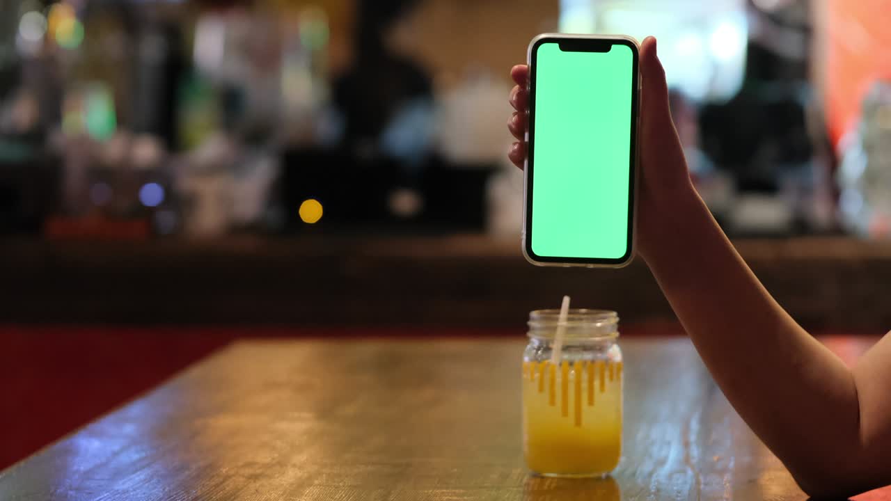 mano mostrando teléfono móvil de pantalla verde en el bar.