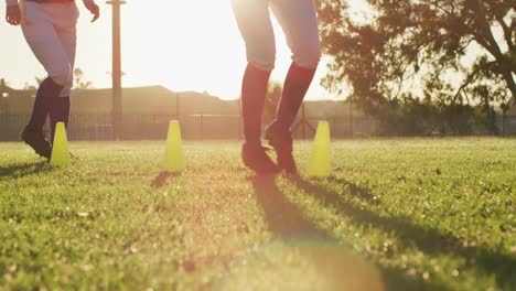 grupo diverso de jugadoras de béisbol ejercitándose en un campo soleado, corriendo entre conos