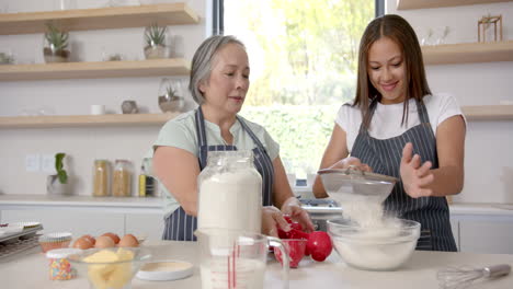 baking together, asian grandmother and granddaughter sifting flour in modern kitchen