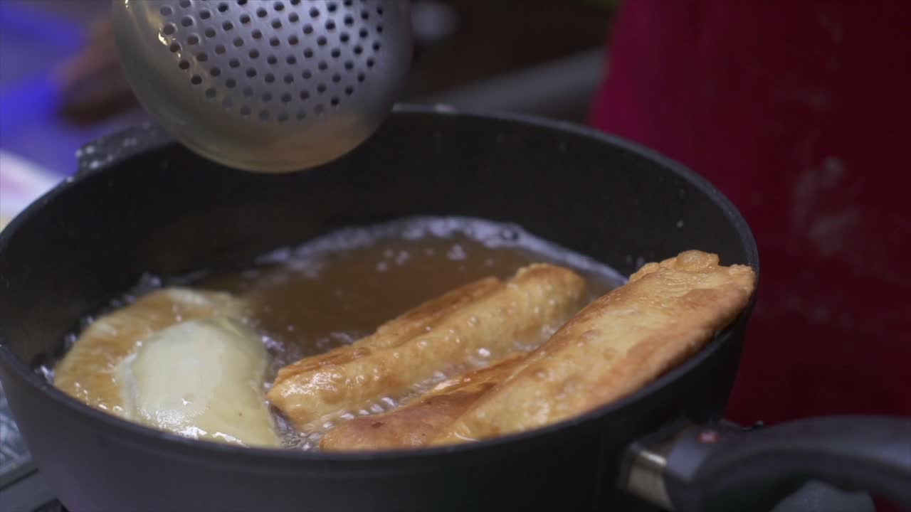Kødrulle og samosa friturestegt og vendt i varm olie, filmet som nærbillede i håndholdt stil.