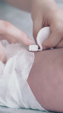 careful nurse hands treat cute little newborn boy with pacifier umbilical cord with cotton pad extreme close view