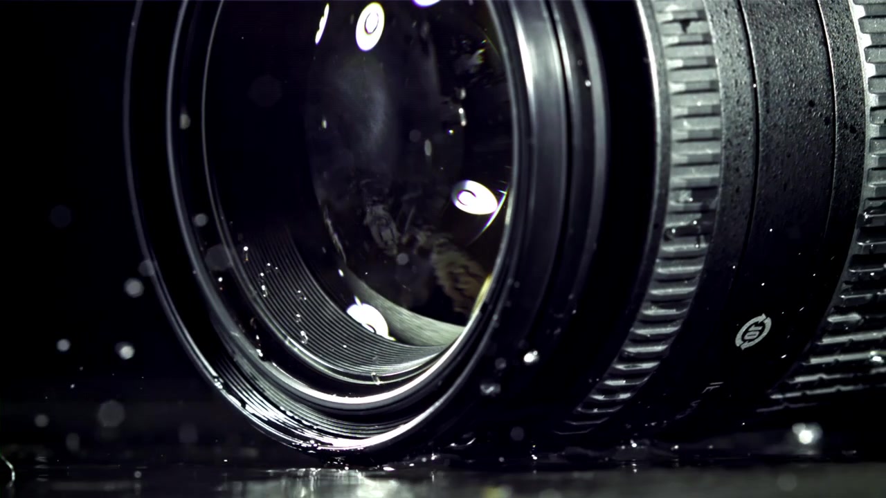 Obiettivo della fotocamera che cade nell'acqua con schizzi, al rallentatore