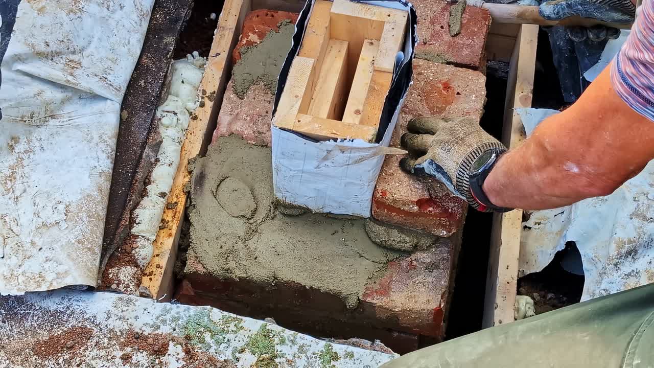 Un muratore che costruisce un camino in mattoni, modellando la malta con un martello e una cazzuola.