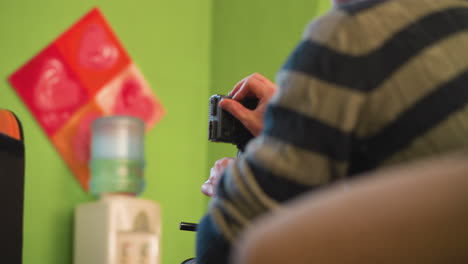 studio guy attaching battery to camera while setting up equipment. focus on hands and camera gear. indoor studio environment with green and orange walls in the background