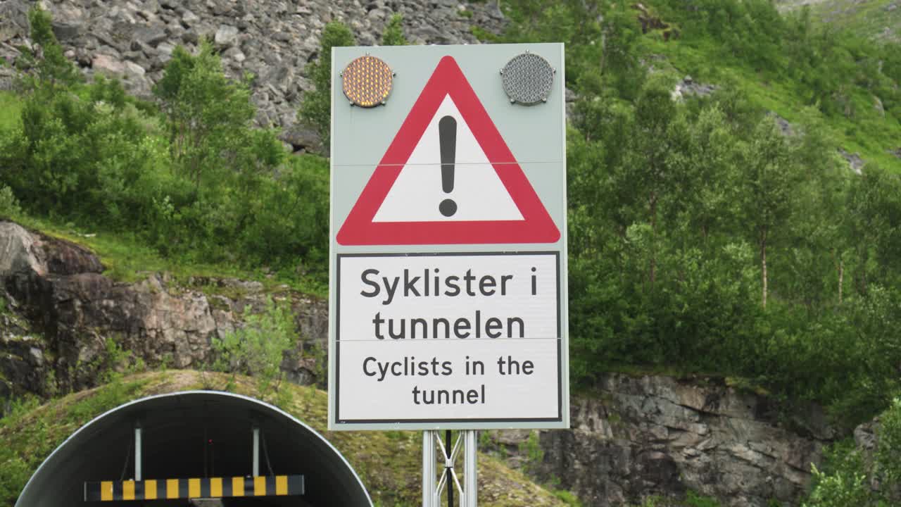 Norveççe ve İngilizce bir uyarı işareti, Skalandtunnelen, Norveç'te tüneldeki bisikletçi. Yakın çekim.